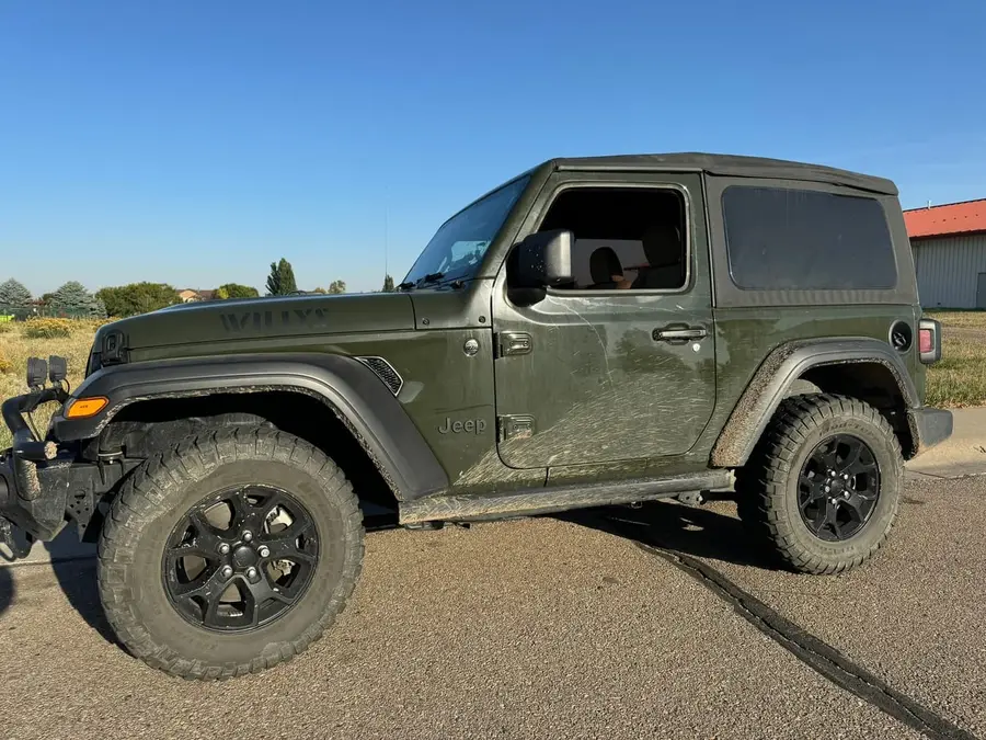 Sarge Green Jeep Wrangler JL Willys two-door, mud-covered, with a soft top and aftermarket front bumper lights