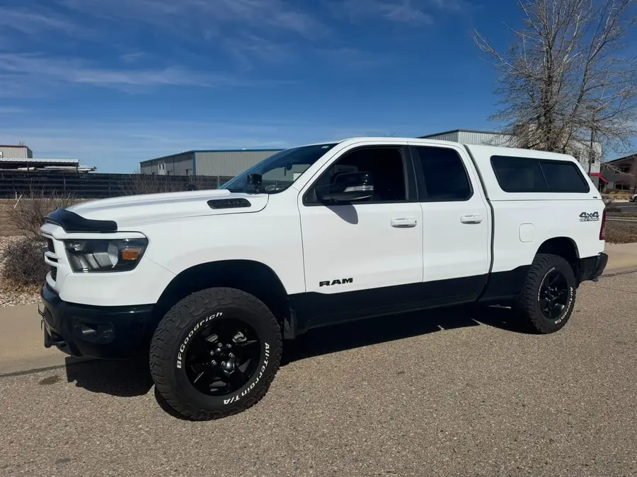 White Ram 1500 with a camper shell on black wheels and all-terrain tires