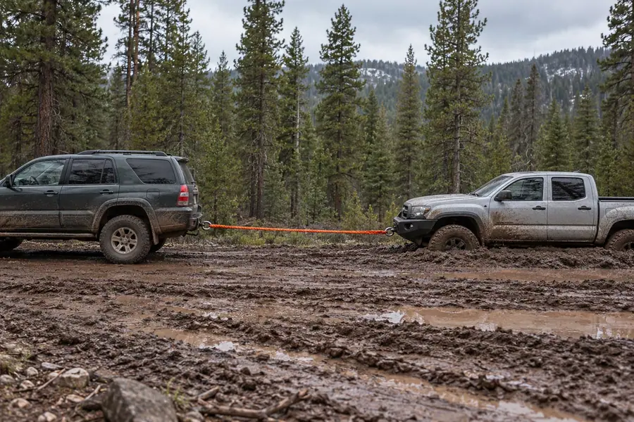 One pickup pulling another out of deep mud with a stretched kinetic rope
