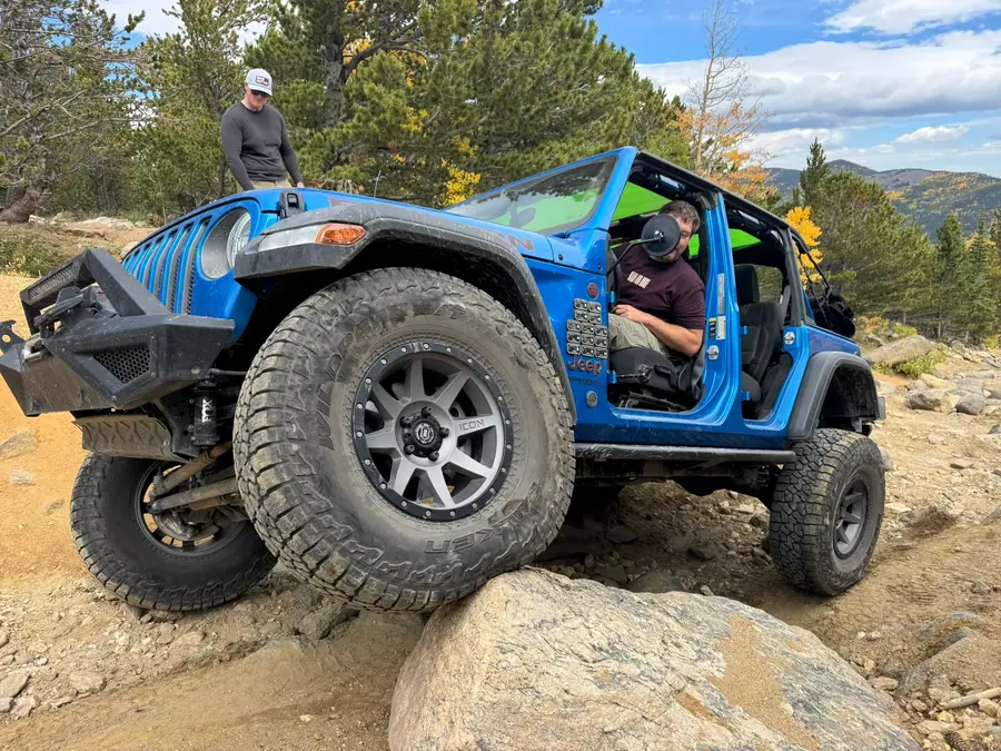 Blue Jeep Wrangler JL stepping up onto a rock with a spotter nearby