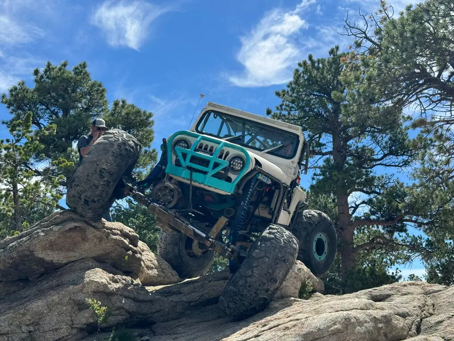 Teal Jeep flexed out on a rock obstacle in the pines