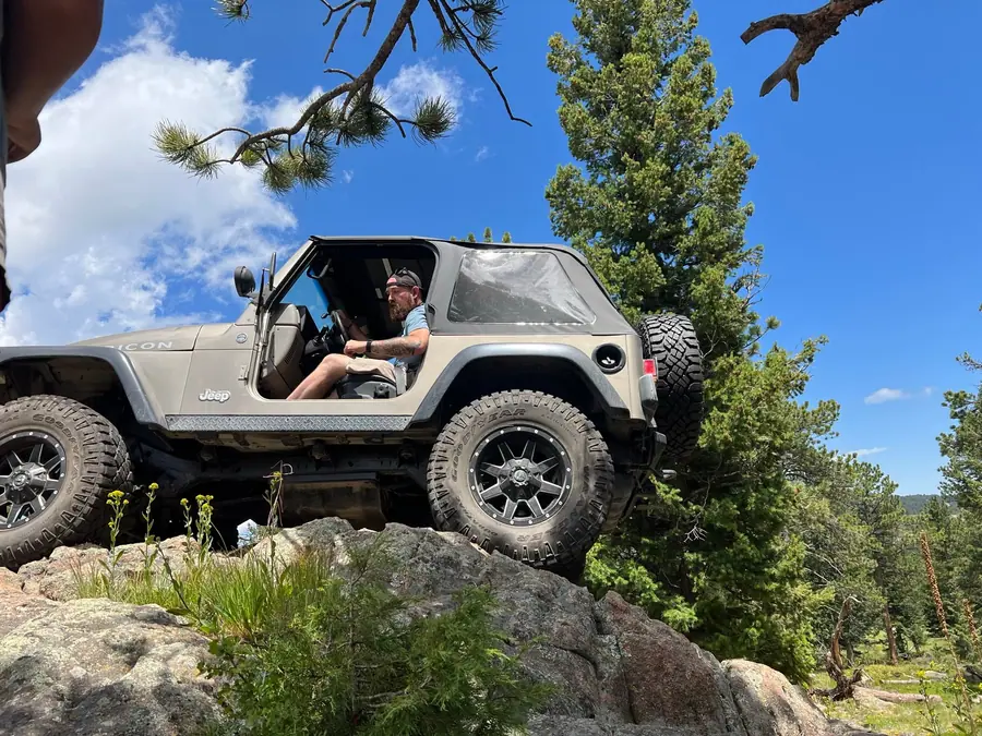 Club member driving a Jeep Gladiator over a rock in the pines