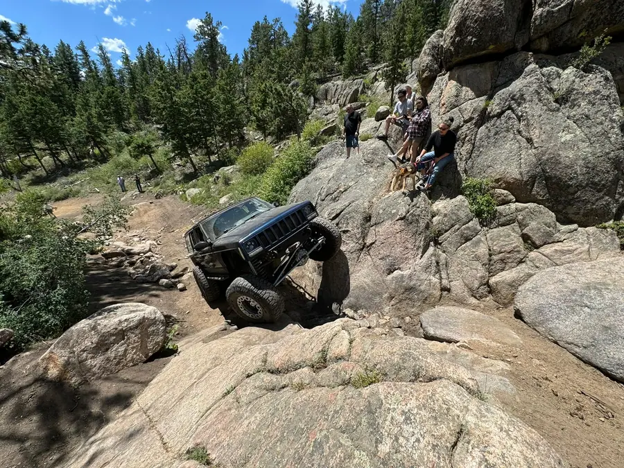 Jeep climbing a granite ledge while club members spot from the rocks