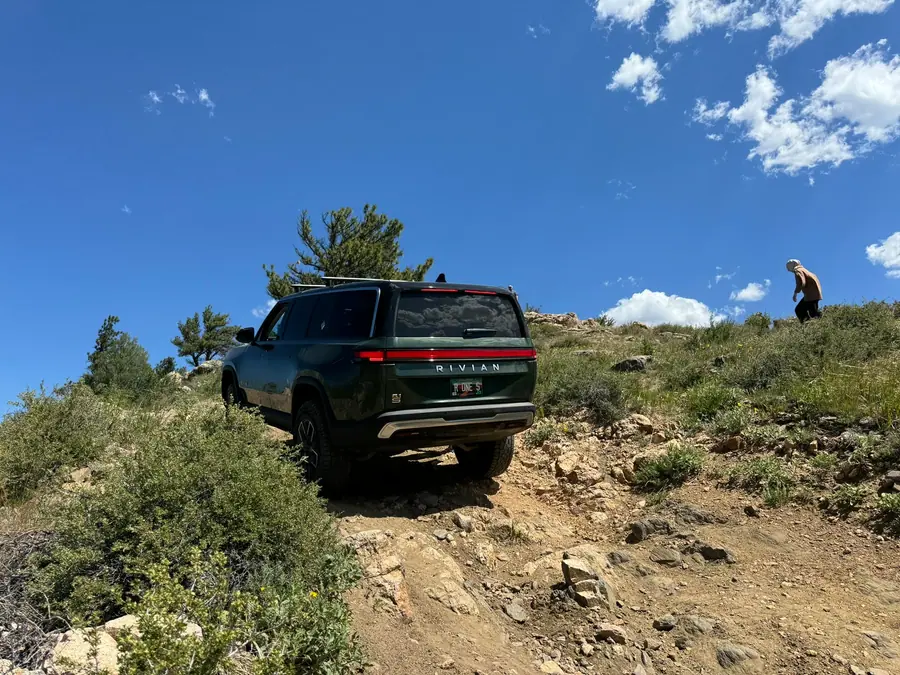 Rivian climbing a steep rocky hill with a club member watching