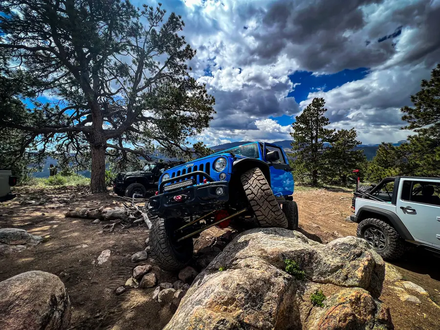 Blue Jeep flexing over boulders at a mountain overlook on a club run