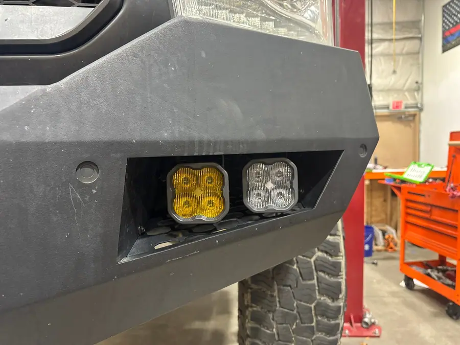 SAE yellow fog pod beside a white driving pod in a steel front bumper