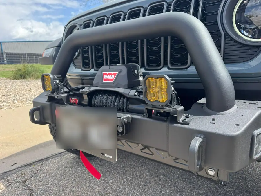 Two SAE yellow Diode Dynamics SS5 LED pods mounted on a steel front bumper beside a Warn winch on a 2024 Jeep Wrangler