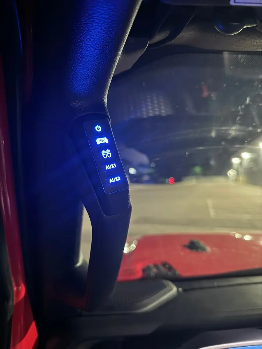 Backlit A-pillar switch panel with labeled light bar, pod and auxiliary circuits in a Jeep at night