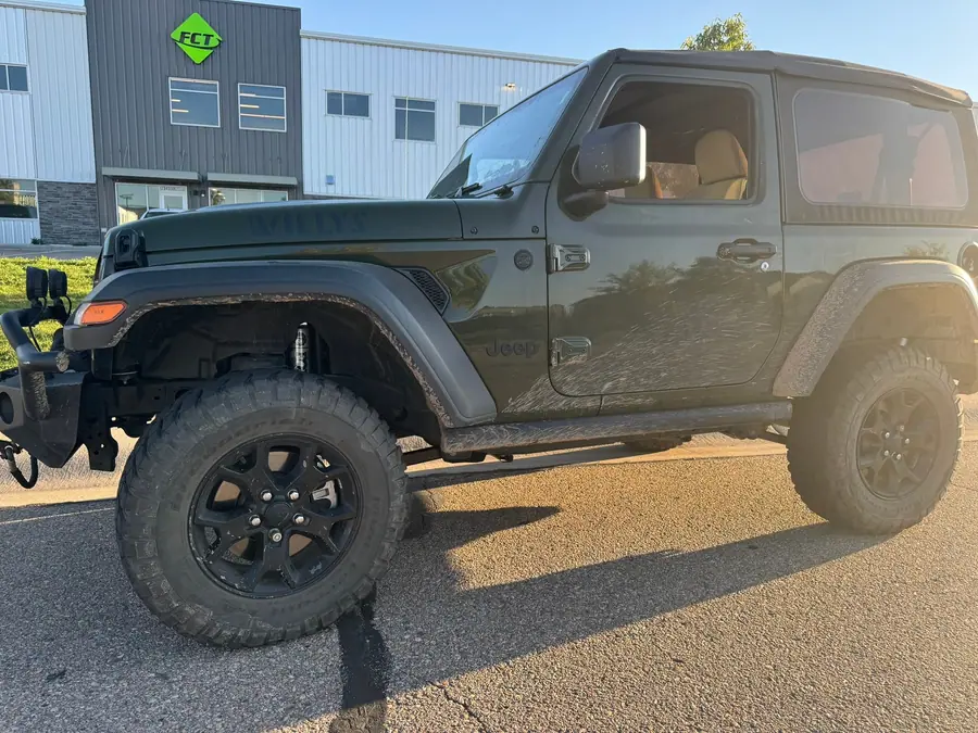 Lifted green two-door Jeep Wrangler JL on black wheels and mud-terrain tires